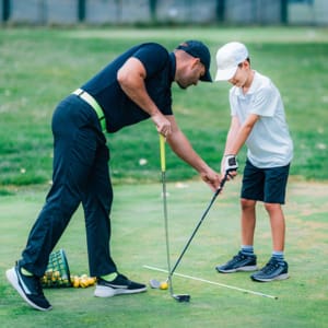Golf Lessons. A golf Instructor and a boy practicing on a Golf Practice Range golflektion med instruktor